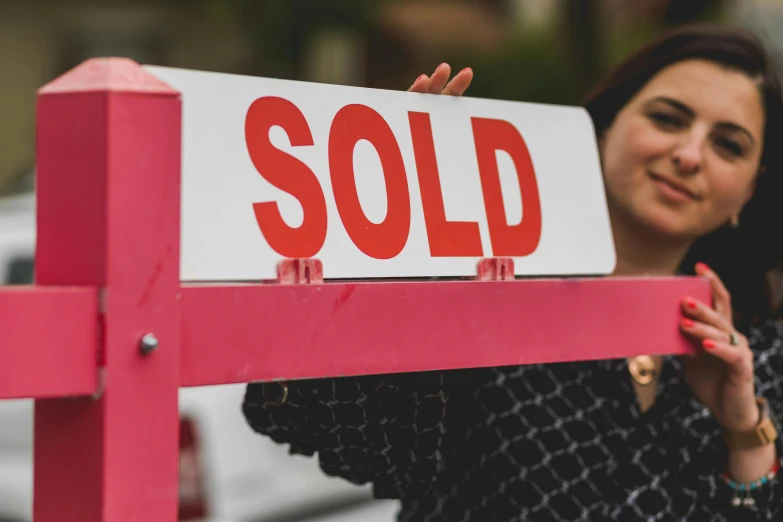 a woman standing in front of a sold sign, pexels contest winner, square, thumbnail, up-close, real estate photography