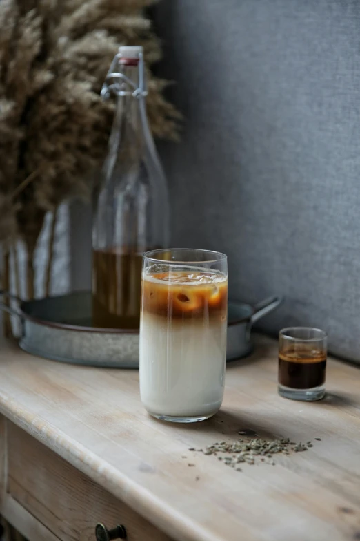 a glass of coffee sitting on top of a wooden table, inspired by Ceferí Olivé, hurufiyya, iced latte, thumbnail, seeds, white