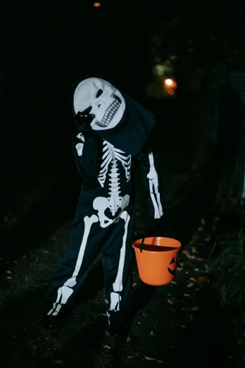 a person in a skeleton costume holding a bucket, profile image, 2019 trending photo, kid, night outside