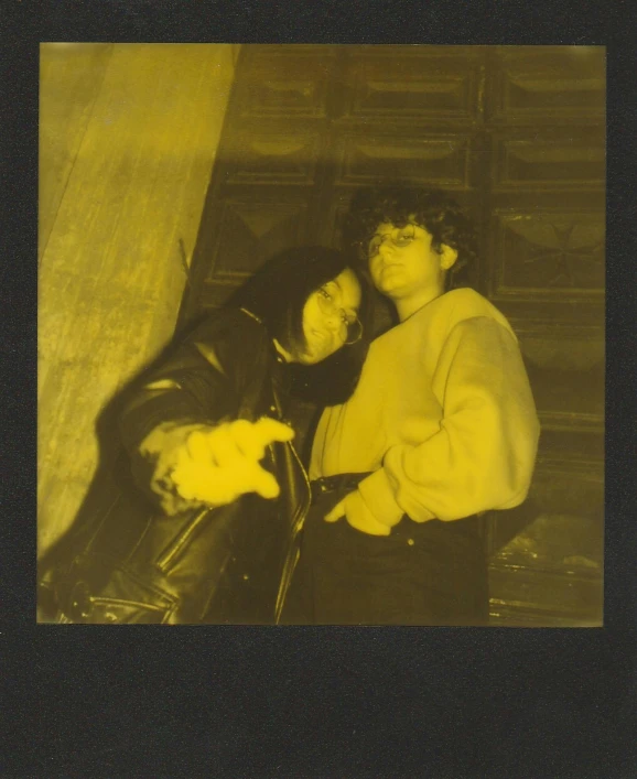 a couple of people standing next to each other, a polaroid photo, inspired by Nan Goldin, vanitas, yellow tint, in a black hoodie, declan mckenna, monocolor