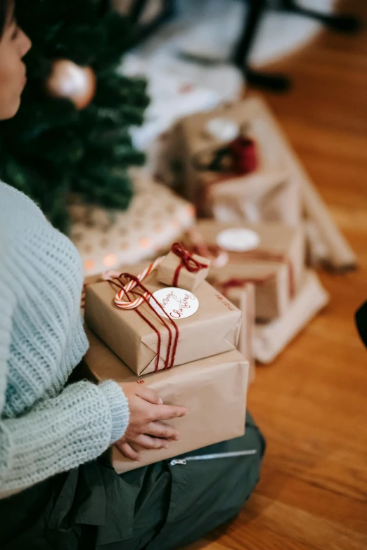 a woman sitting on the floor in front of a christmas tree, giving gifts to people, brown paper, subtle detailing, manuka