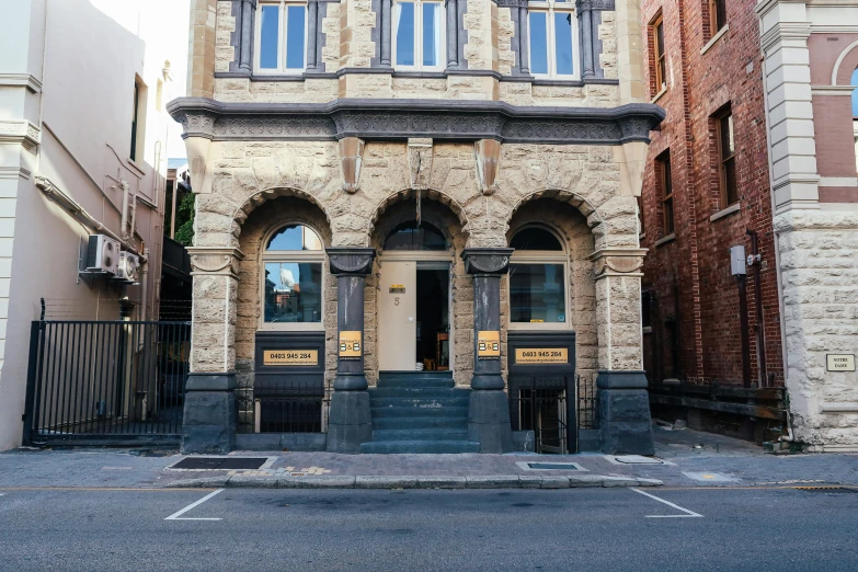 a tall building sitting on the side of a street, tall arched stone doorways, north melbourne street, golden hues, saloon exterior
