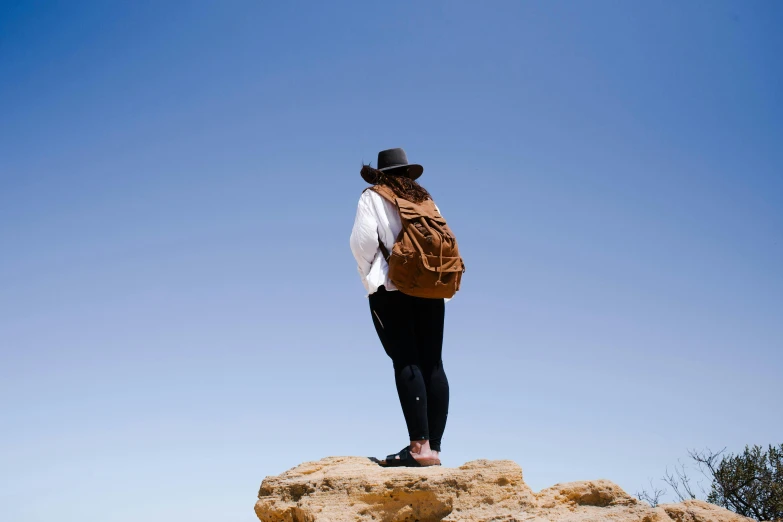 a person with a backpack standing on a rock, by Lee Loughridge, happening, woman with hat, caramel. rugged, on a hot australian day, looking to the sky