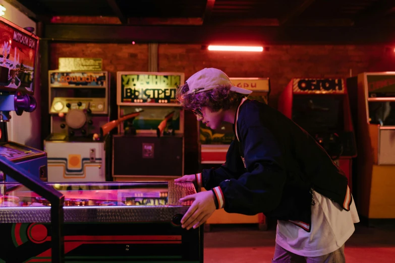 a man standing in front of a pinball machine, pexels contest winner, finn wolfhard, playing games, neon lights above shops, lachlan bailey