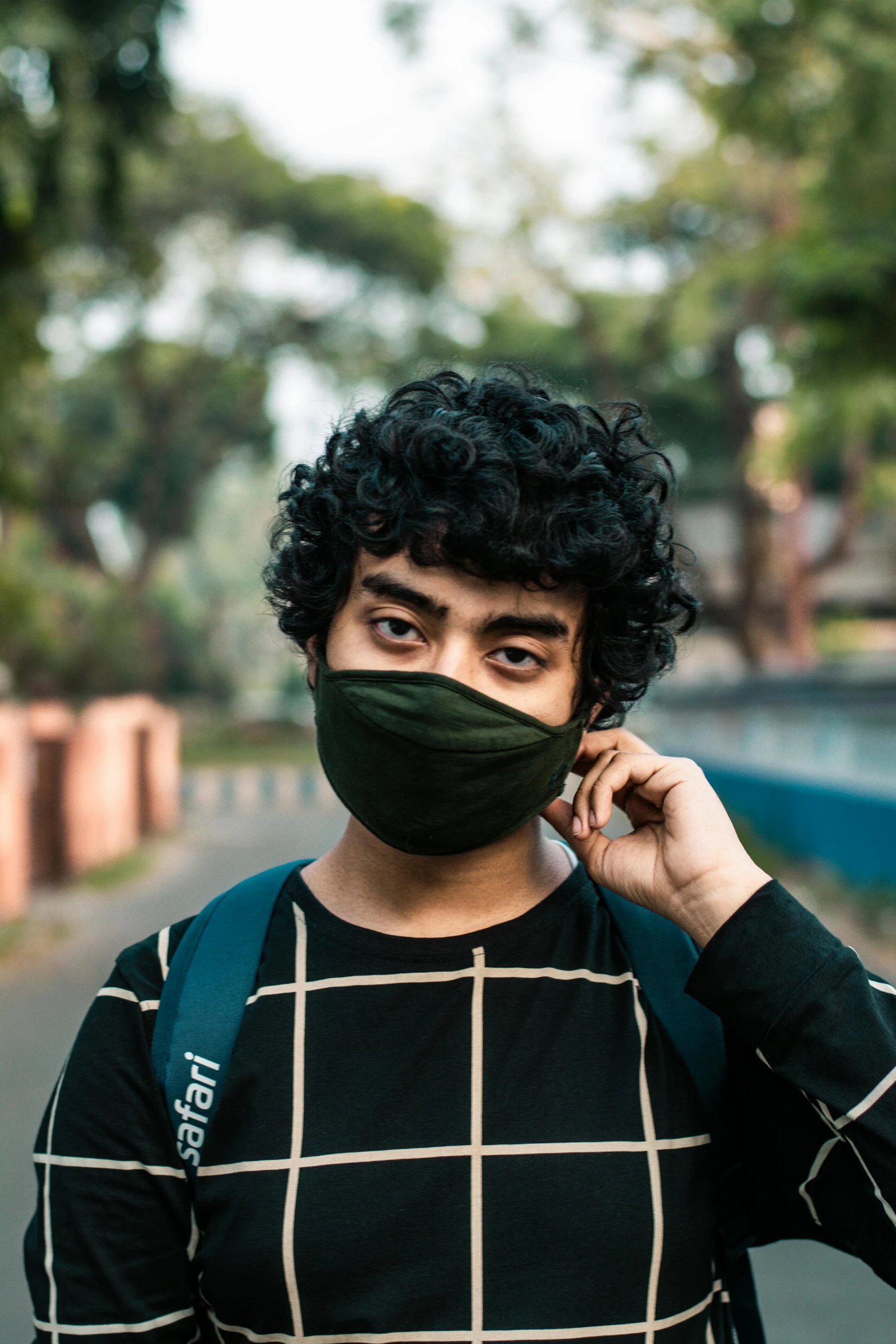 a man wearing a face mask while talking on a cell phone, an album cover, trending on pexels, bangladesh, short black curly hair, student, it\'s name is greeny