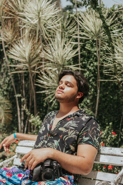 a man sitting on a bench with a camera, palm trees in the background, asher duran, eyes closed, lean man with light tan skin