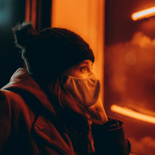 a woman wearing a face mask on a train, by Adam Marczyński, pexels contest winner, orange neon backlighting, cold winter, warm street lights store front, dim red light