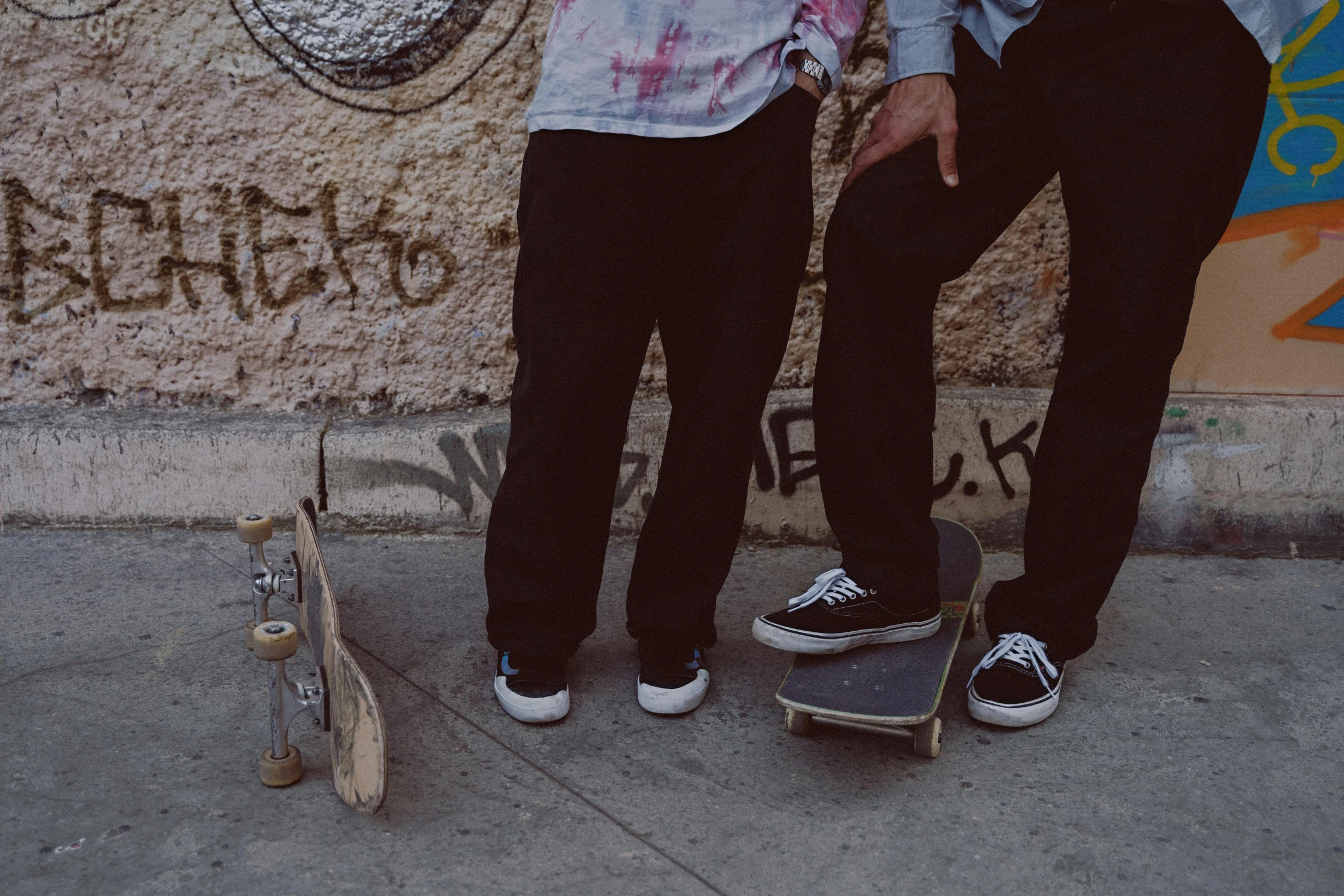 two people standing next to a wall with graffiti on it, a picture, unsplash, graffiti, detailed skateboard, brothers, pants, 15081959 21121991 01012000 4k