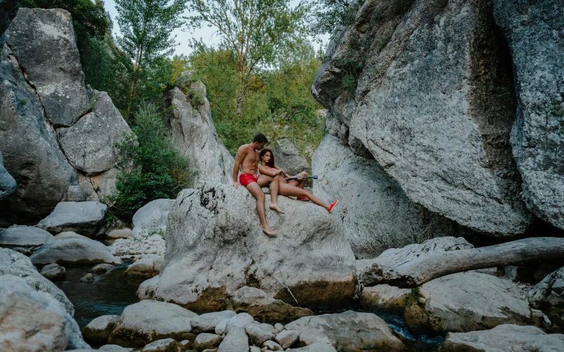 a man and a woman sitting on a rock in a river, by Raphaël Collin, pexels contest winner, figuration libre, wearing red shorts, ashteroth, al fresco, with full descriptions