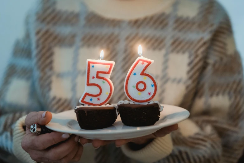 a woman holding a plate of cupcakes with lit candles, by Emma Andijewska, trending on unsplash, figuration libre, 5 0 years old man, golden number, emma bridgewater and paperchase, 65mm