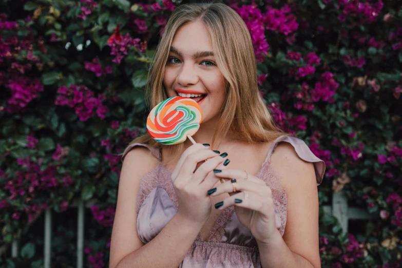 a woman holding a lollipop in front of her face, a colorized photo, by Emma Andijewska, pexels contest winner, smiling young woman, 🐿🍸🍋, sydney sweeney, painted nails