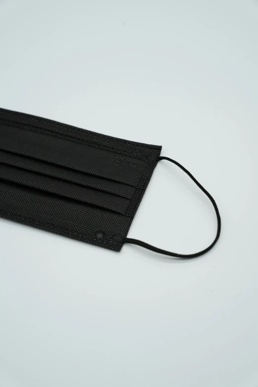 a black face mask on a white surface, coated pleats, product introduction photo, surgical supplies, main colour - black