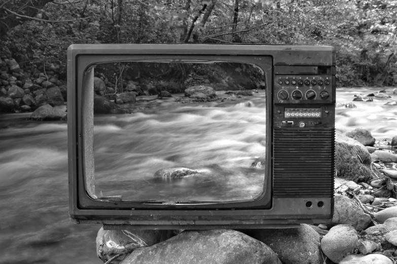 an old television sitting on top of a pile of rocks, a black and white photo, inspired by Ansel Adams, pixabay, video art, river running through it, panel, creek, watching tv
