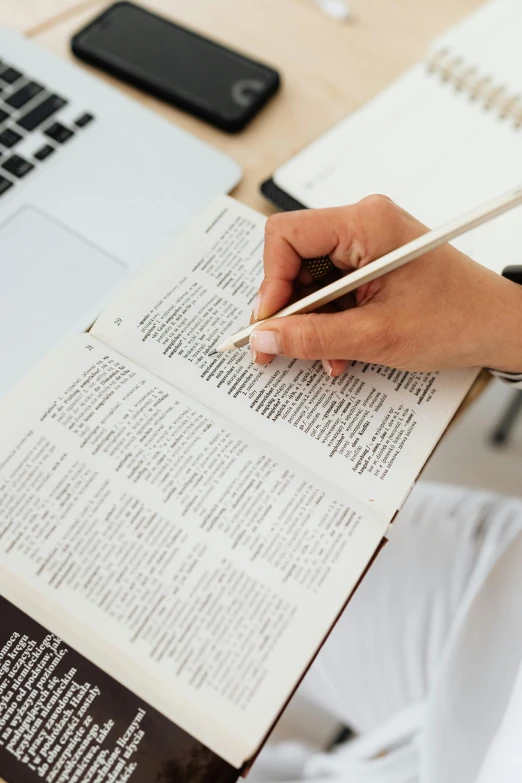 a person sitting at a desk with a laptop and a book, biblical, thumbnail, holding pencil, multiple stories