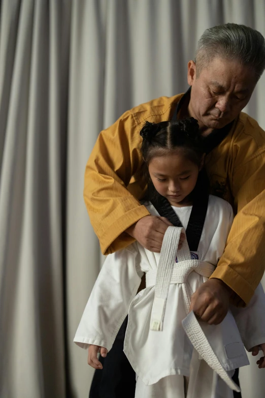 a man standing next to a little girl in a kimono, inspired by Kanō Shōsenin, unsplash, aikido, film still promotional image, inuit heritage, yellow robes