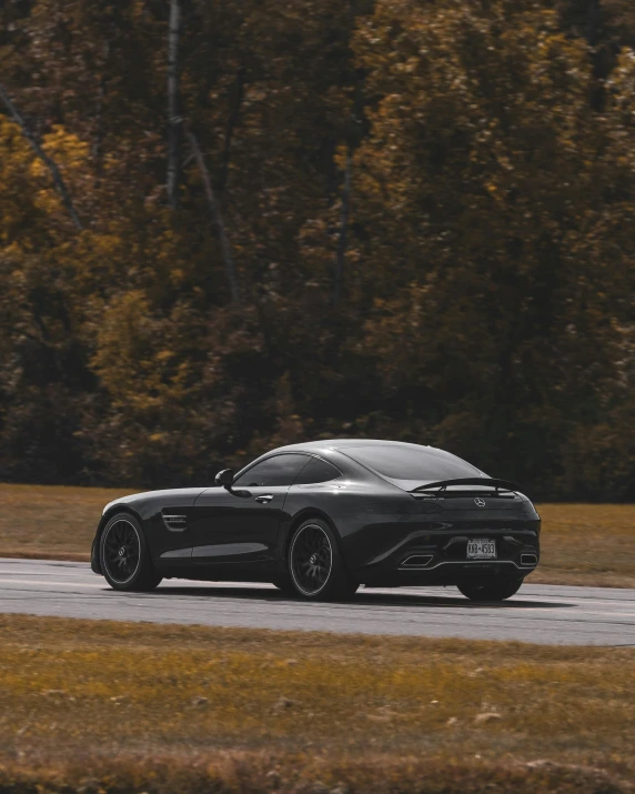 a black sports car driving down a road, in front of a forest background, trending on vsco, on a racetrack, fall season