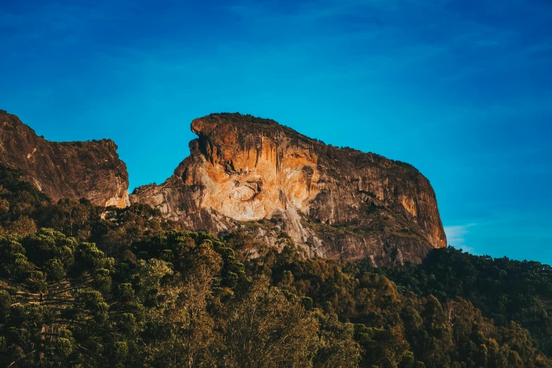 a large rock in the middle of a forest, by Lee Loughridge, unsplash contest winner, blue and clear sky, tamborine, giant imposing mountain, avatar image