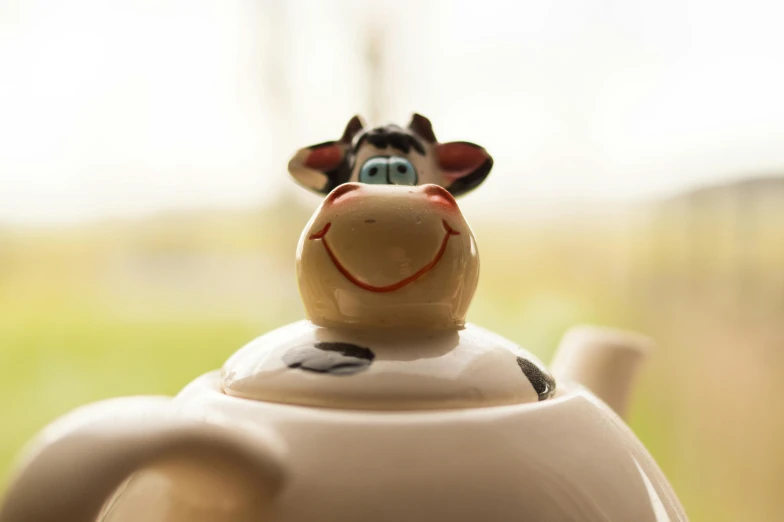 a cow figurine sitting on top of a teapot, inspired by Tex Avery, unsplash, closeup face, aardman, smiling, eye level view