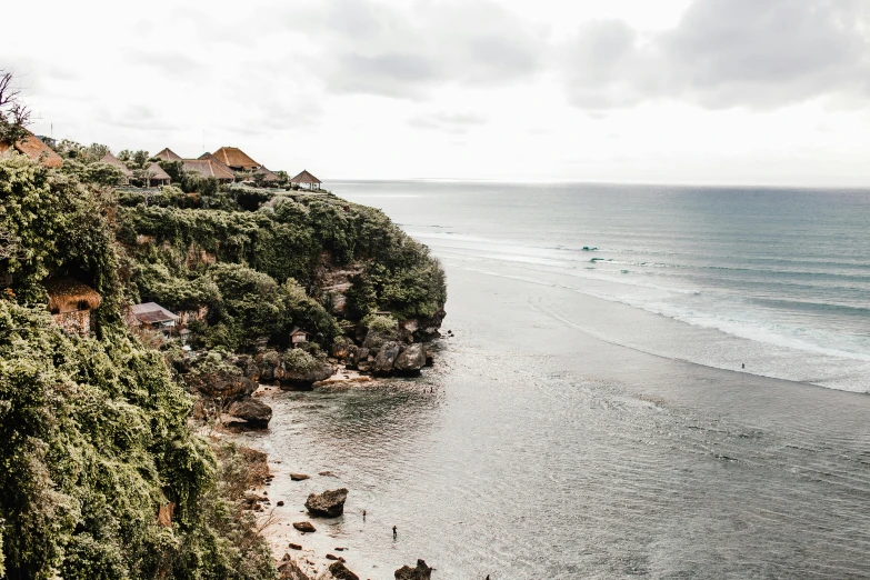 a man standing on top of a cliff next to the ocean, bali, flatlay, small cottage in the foreground, mermaids in distance