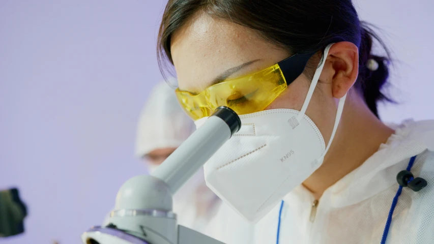 a woman in a lab coat looking through a microscope, pexels contest winner, white and purple, surgical mask covering mouth, profile image, uniform teeth