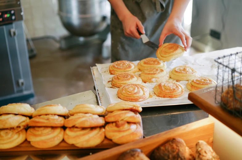 a person standing in front of a counter filled with pastries, inspired by Richmond Barthé, trending on pexels, snails, australian, organic rippling spirals, slightly sunny