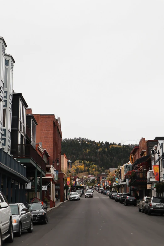 a street lined with parked cars next to tall buildings, renaissance, colorado mountains, storefronts, muted fall colors, top of the hill