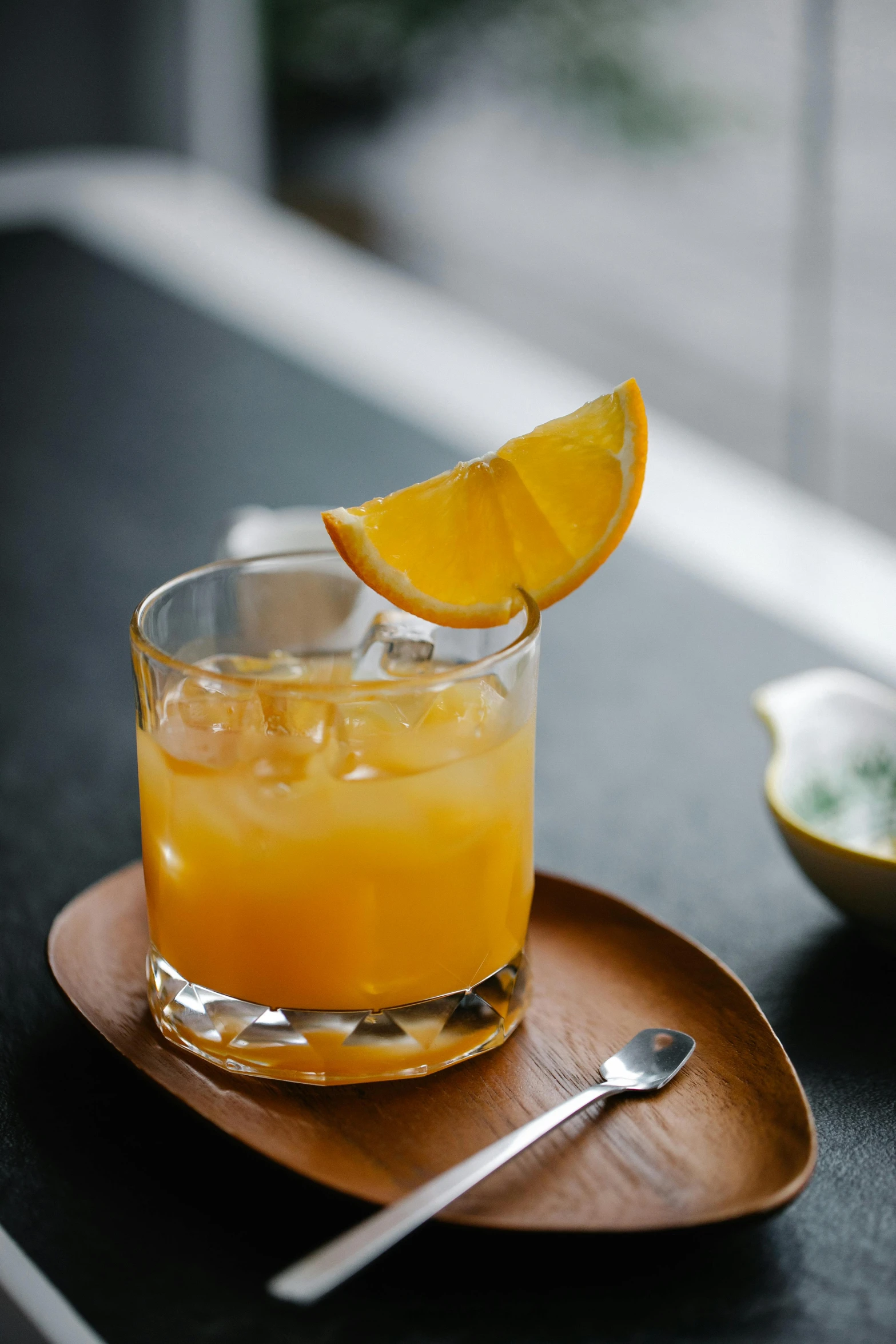 a glass of orange juice sitting on top of a wooden plate, inspired by Kanō Shōsenin, renaissance, rum, square, uncropped, grey orange