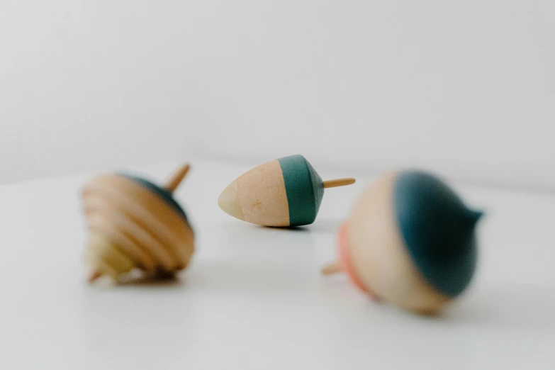 three wooden acorns sitting on top of a table, an abstract sculpture, unsplash, toys, teal, spinning, in muted colours