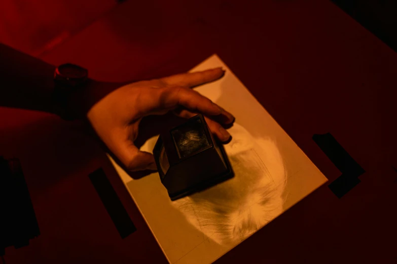 a close up of a person holding a cell phone, by Daniel Lieske, holography, lit. 'the cube', séance, red ink, on a table