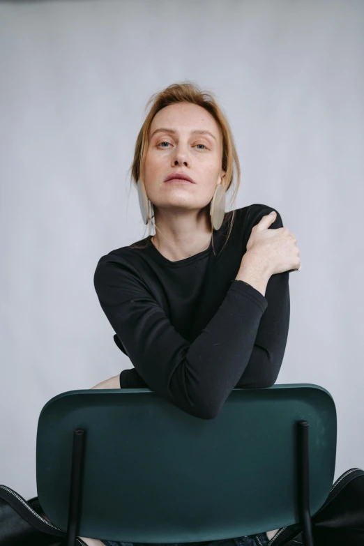 a woman sitting on top of a green chair, by Attila Meszlenyi, trending on unsplash, renaissance, wearing a black sweater, in front of white back drop, wearing a black tshirt, olya bossak