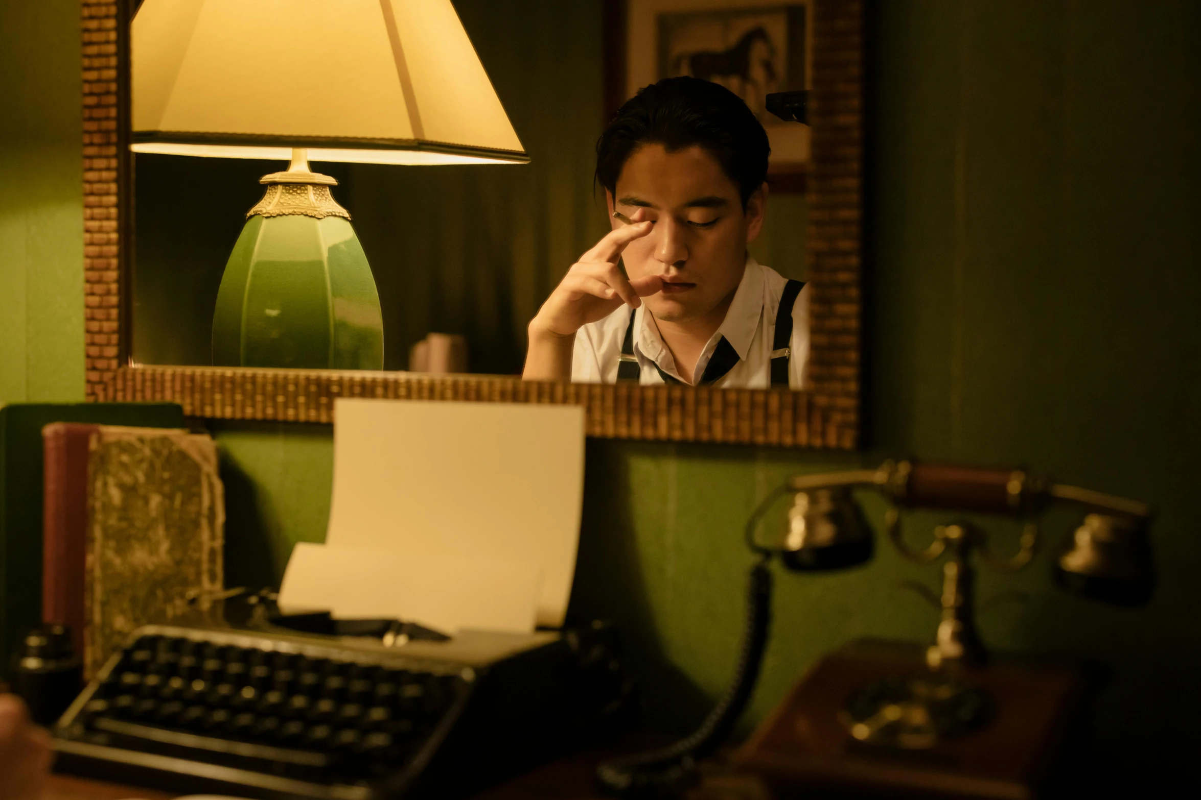 a man sitting at a desk with a typewriter, a portrait, by Elsa Bleda, unsplash, serial art, korean film noir, 8 k movie still, holding up a night lamp, with a sad expression