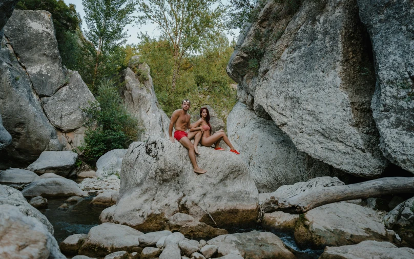 a man and a woman sitting on a rock in a river, by Raphaël Collin, pexels contest winner, figuration libre, wearing red shorts, naturist, in a valley, bad camrea