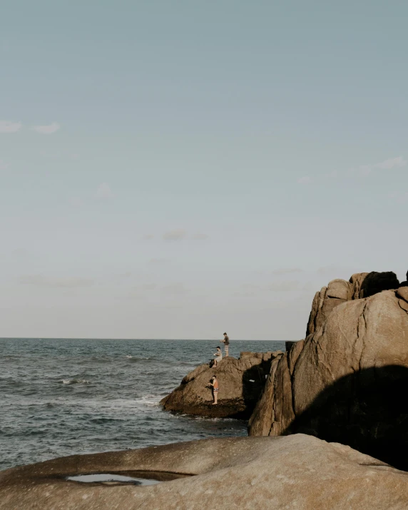 a man standing on top of a rock next to the ocean, lgbtq, people angling at the edge, trending photo, in the distance is a rocky hill