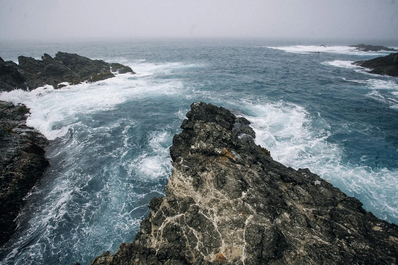 a large body of water next to a rocky shore, an album cover, pexels contest winner, low pressure system, azores, low quality photo, grey