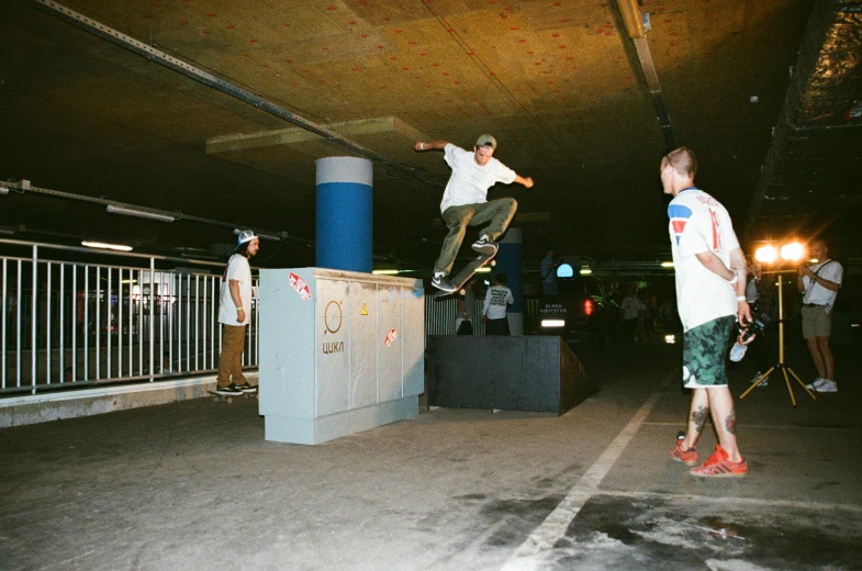 a man flying through the air while riding a skateboard, a picture, unsplash, graffiti, in an underground parking garage, lots of people, 2000s photo, summer night