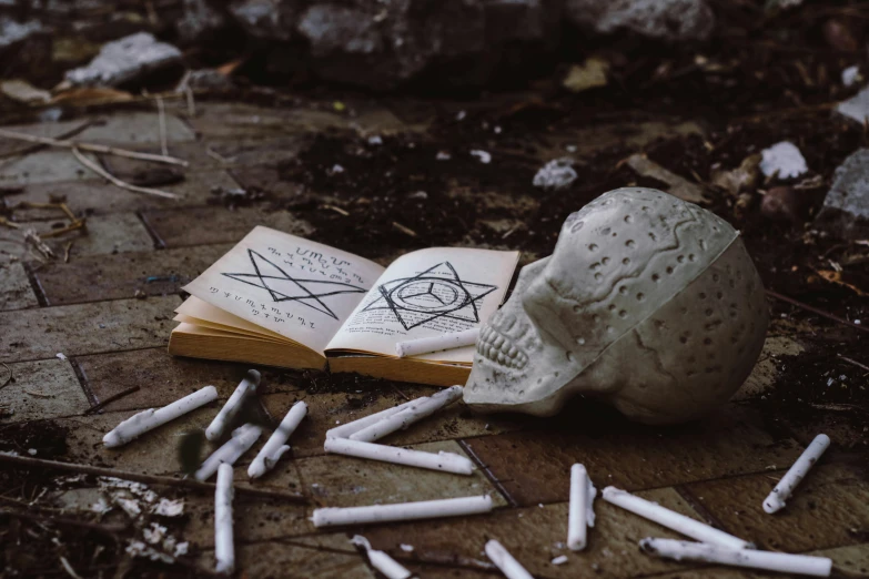 an open book sitting on top of a pile of cigarettes, a charcoal drawing, pexels contest winner, gothic art, skulls on the ground, pentagrams, instagram photo, with a creepy secret temple