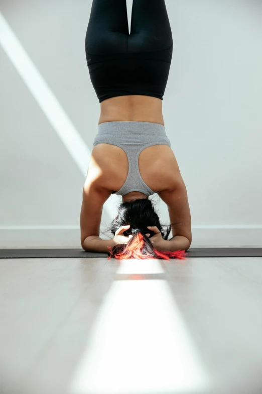 a woman doing a handstand on a yoga mat, pexels contest winner, light and space, wearing tumultus flames, cropped red yoga short, grey, lizard pose