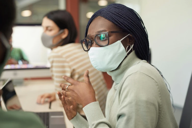 a woman wearing a face mask sitting at a desk, trending on pexels, standing in class, avatar image, calmly conversing 8k, close - up photo