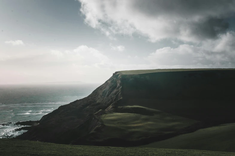 a couple of sheep standing on top of a lush green hillside, by Colin Middleton, unsplash contest winner, coastal cliffs, moody hazy lighting, a round minimalist behind, sweeping vista