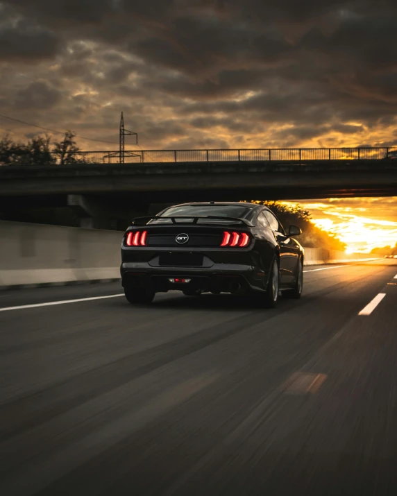 a black mustang driving down a highway at sunset, unsplash contest winner, lgbtq, back arched, low quality photo, profile image