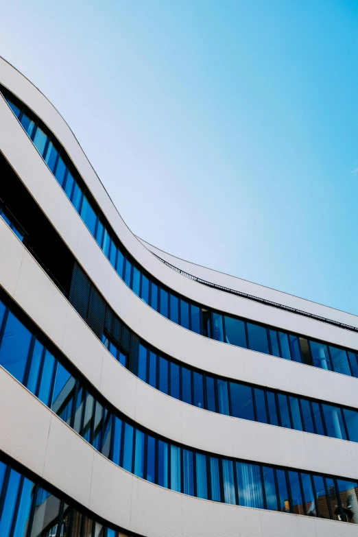 a tall building with many windows in front of a blue sky, inspired by Zaha Hadid, unsplash, rounded roof, alvar aalto, white and blue, austrian architecture