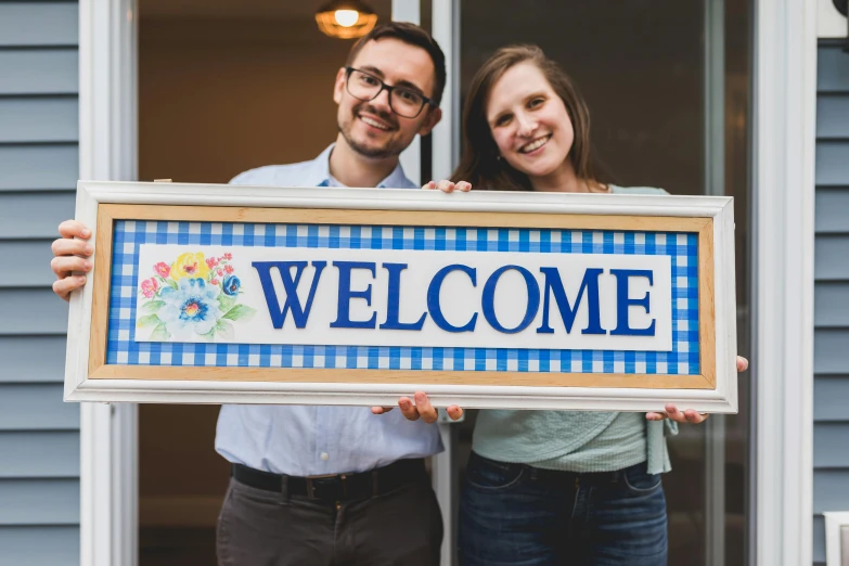 a man and a woman holding a welcome sign, pexels contest winner, folk art, ultra-realistic, at home, profile image, full product shot