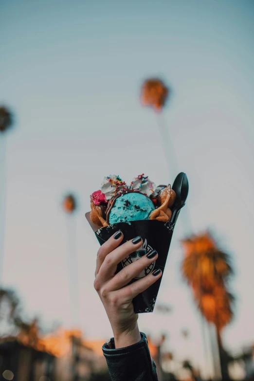 a person holding up an ice cream cone, unsplash contest winner, palm springs, black and blue, edible flowers, late evening