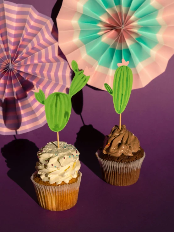 a couple of cupcakes sitting on top of a table, holding a cactus, purple colour scheme, diecut, festivals