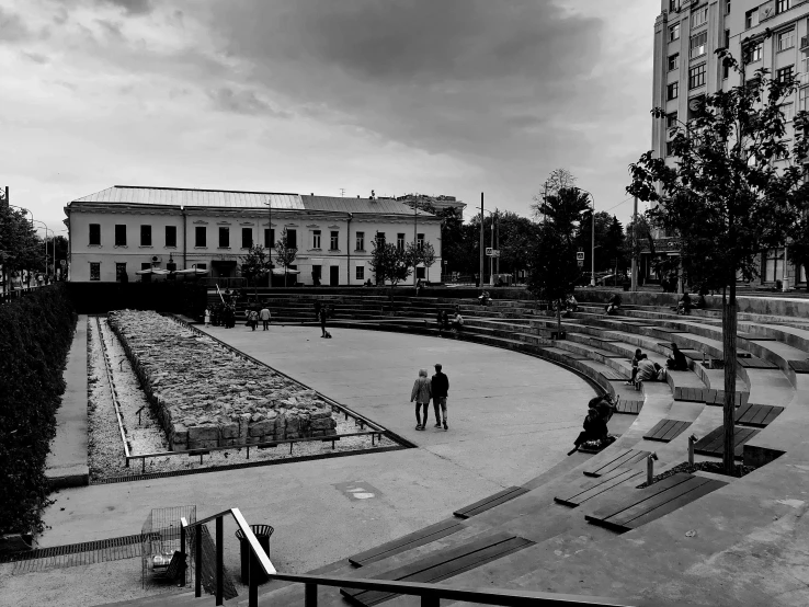 a black and white photo of a skateboard park, socialist realism, lviv historic centre, mini amphitheatre, people resting on the grass, a wide open courtyard in an epic