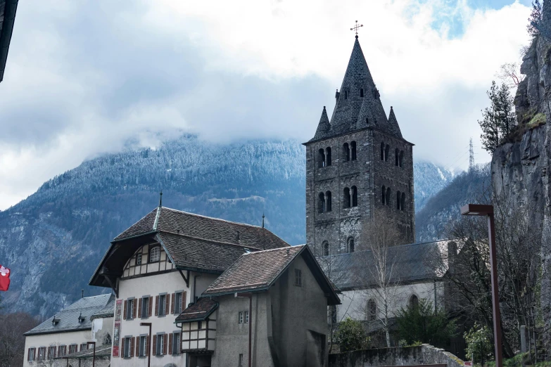 a church in the middle of a town with mountains in the background, a photo, pexels contest winner, romanesque, wintry rumpelstiltskin, rossier, brutalist buildings tower over, gray