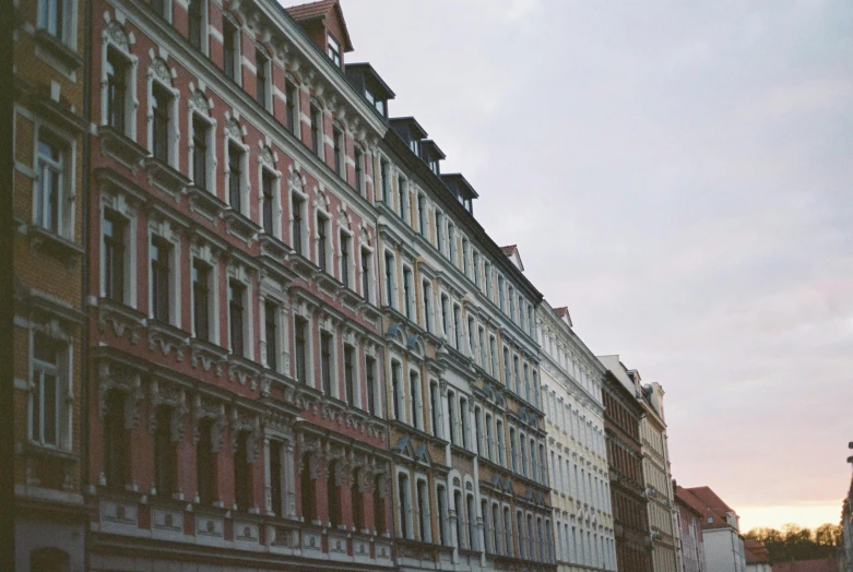 a group of people walking down a street next to tall buildings, a photo, unsplash contest winner, baroque, tenement buildings, kreuzberg, in muted colors, view from the side”