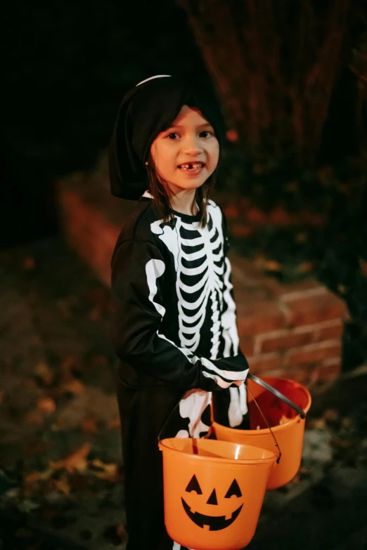 a little girl dressed up in a skeleton costume, a cartoon, by Winona Nelson, pexels, square, dark photo, holding bat, snacks