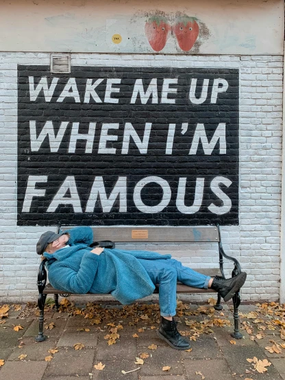a man sleeping on a bench in front of a sign that says wake me up when i'm famous, an album cover, trending on pexels, full body in frame, public art, wearing pajamas, profile image