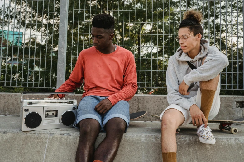 a couple of people sitting on top of a cement wall, trending on pexels, happening, boombox, black teenage boy, still image from tv series, sitting on bench